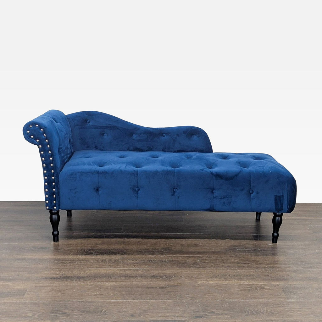 1. Blue velvet chaise lounge with button-tufted seat, silver studs, and sturdy wooden legs on a wooden floor.
