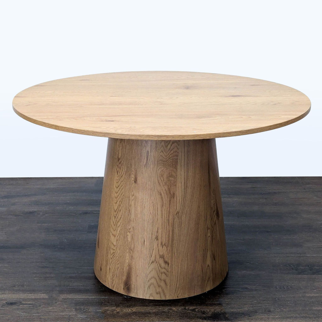 2. Light wood circular dining table featuring a wide cylindrical pedestal, displayed at an angle.
