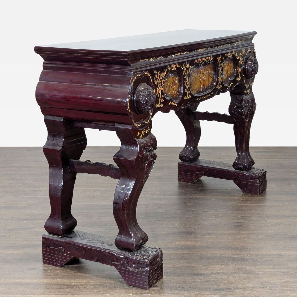 Carved side table with stylized deity legs, detailed panels, two drawers, and shimmering inlaid designs.