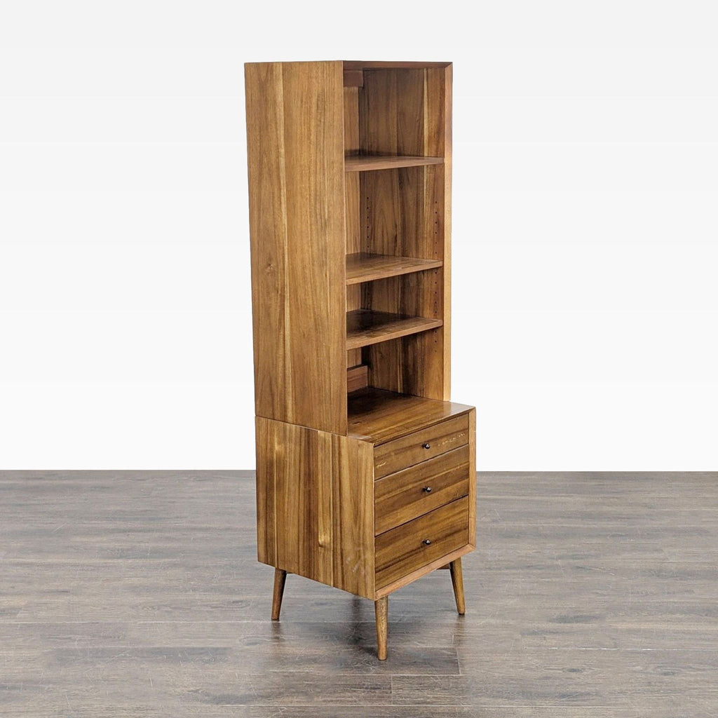 2. Angled view of a wooden West Elm bookshelf featuring open shelves and three lower drawers.  