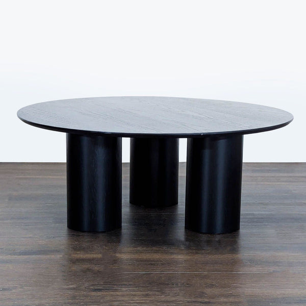 Round drum-style wooden coffee table by Ivy Bronx with bold block legs and modern architectural design.