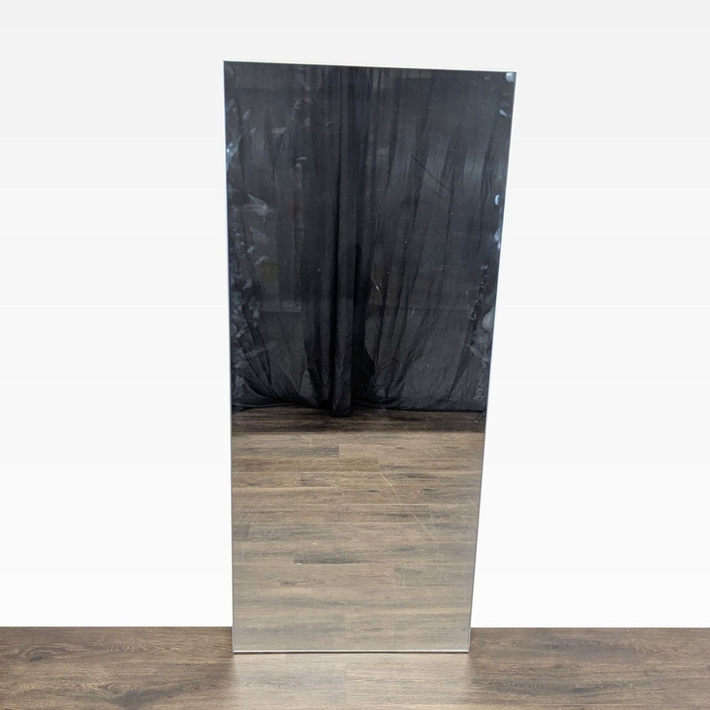 1. Rectangular CB2 floor mirror with a minimalist design, reflecting wood flooring and a black curtain backdrop.