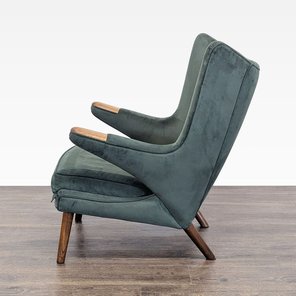 3. Profile view of Hans Wegner lounge chair with soft dark green fabric and wooden armrests, ideal for relaxing.