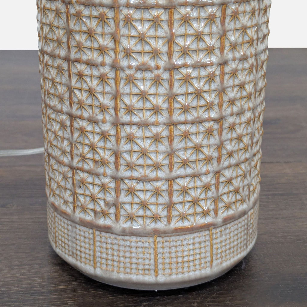 Textured geometric ceramic lamp in beige and brown with fabric shade, fitting for various room decors.