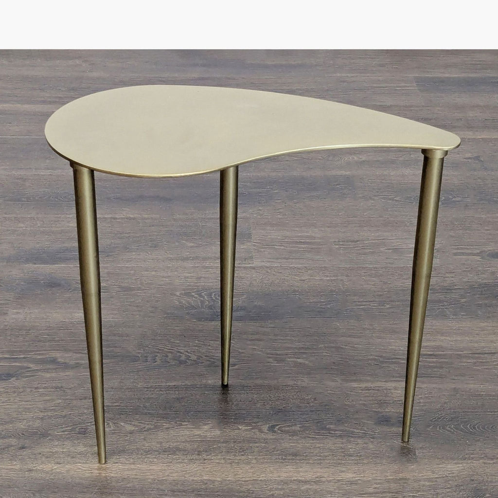 1. Modern side table with gold, kidney-shaped top and three slim legs, shown on a wood floor.  