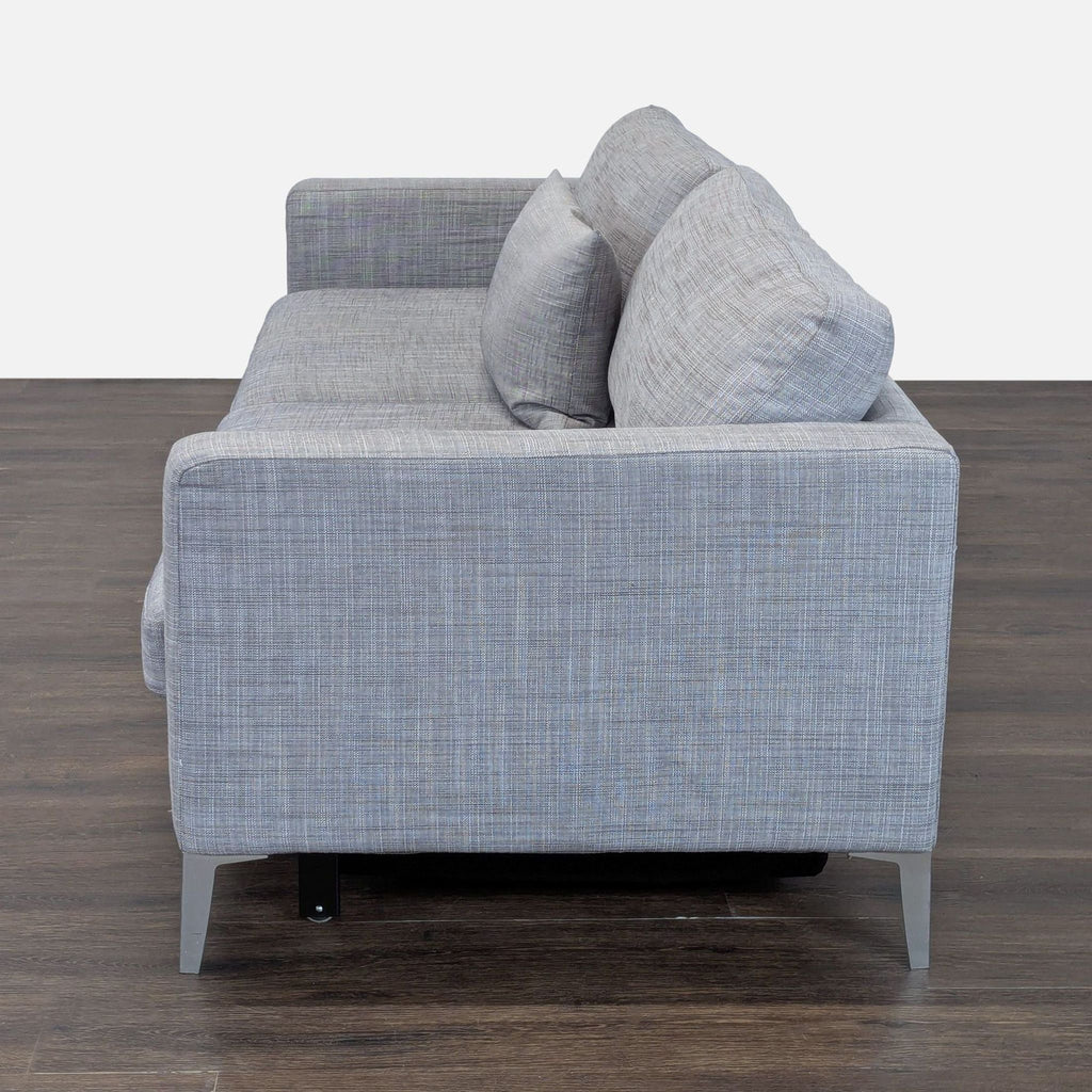 Modern gray sofa that easily transforms into a bed; features sleek lines and a cozy pillow.