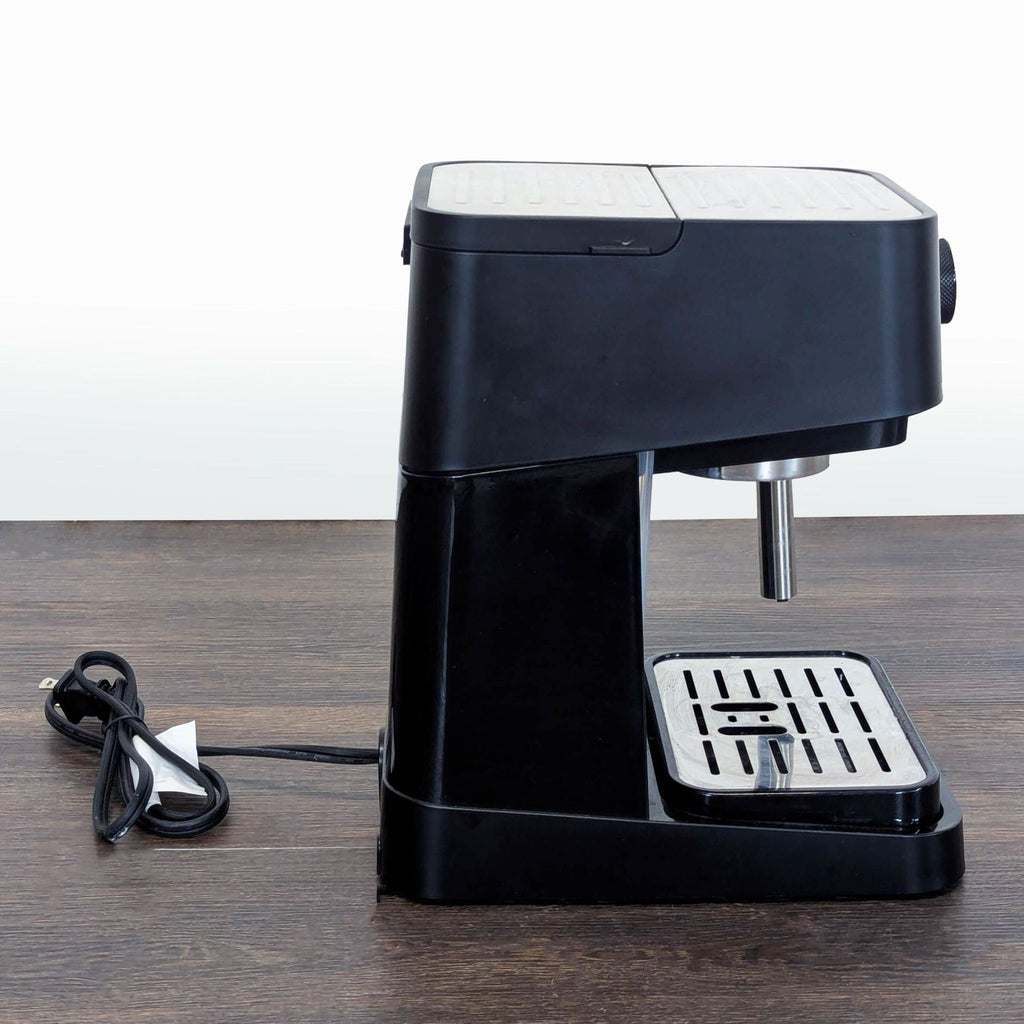 3. Side profile of DeLonghi coffee maker showing the black body, silver top, and attached power cord on a table.