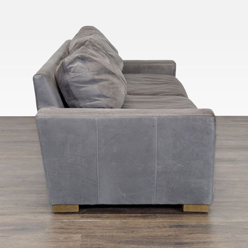 Side view of a Restoration Hardware 3-seat sofa in gray leather, highlighting its wide armrest and durable structure.