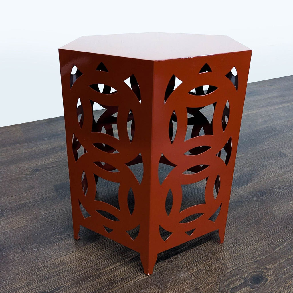 3. Decorative end table with a hexagonal top and bold circular cutouts in a reddish finish, on dark flooring.