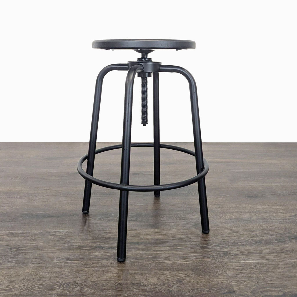 3. Black adjustable-height stool with circular footrest, flat round seat, and four metal legs on a wood floor.