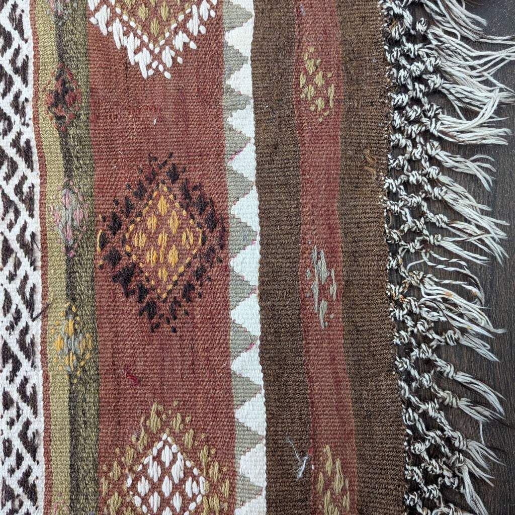 2. Close-up of a handwoven rug corner showing intricate diamond motifs in warm colors and white fringe detail.  