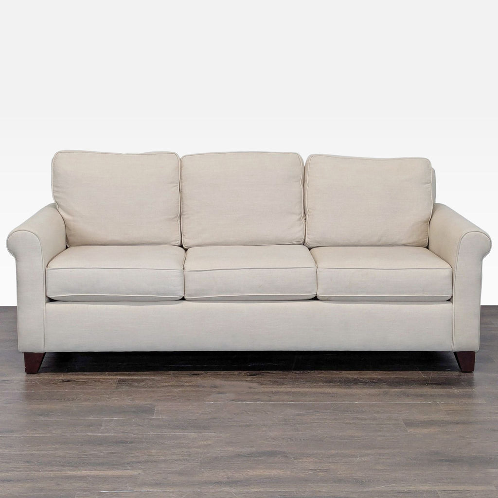 Beige Pottery Barn sofa with rolled arms, removable cushions, and wooden legs seating three people.