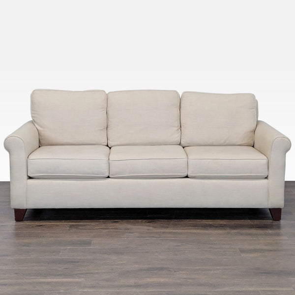 Beige Pottery Barn sofa with rolled arms, removable cushions, and wooden legs seating three people.