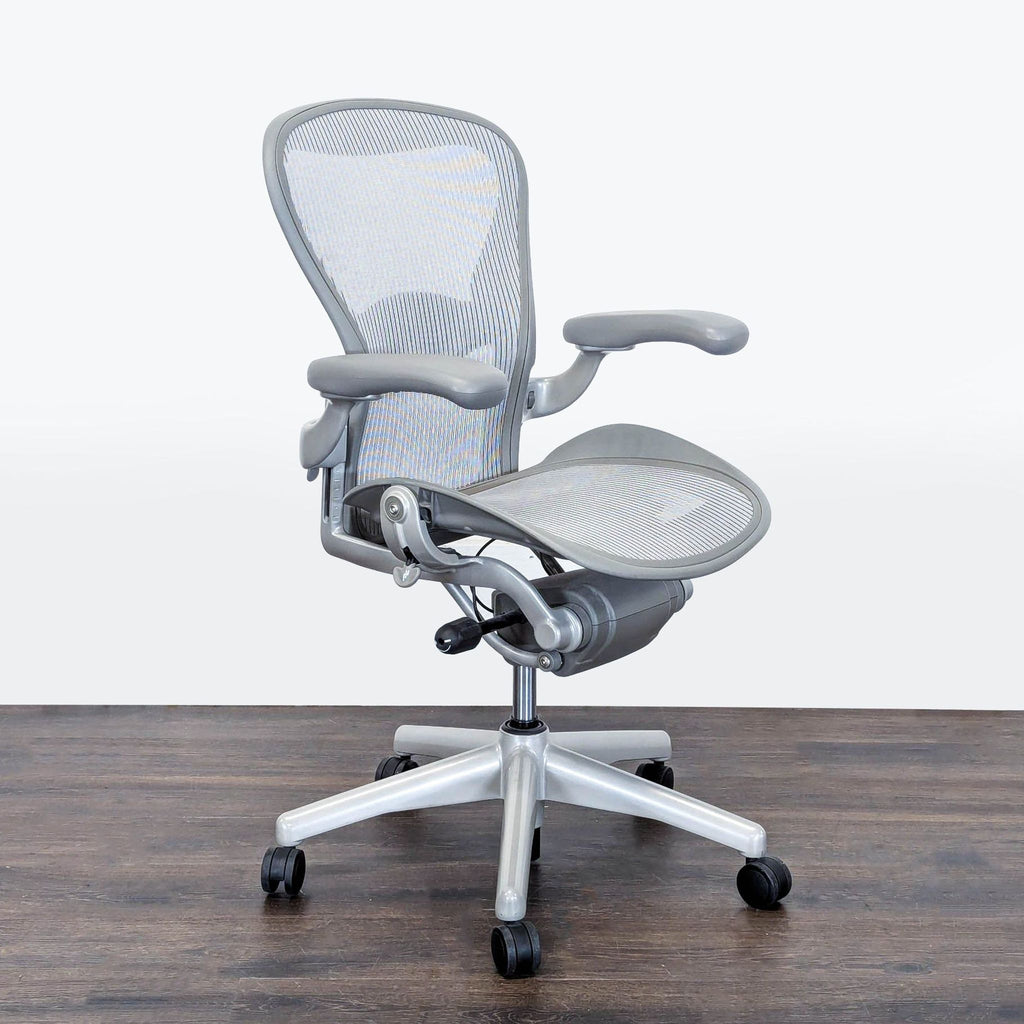 Angled side-front view of the ergonomic Herman Miller Aeron chair, featuring mesh seat, armrests, and sturdy base.