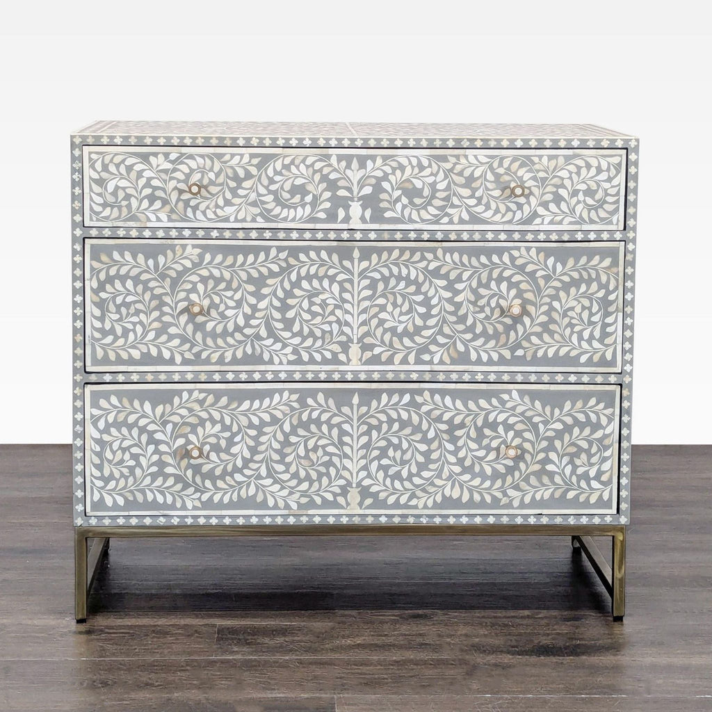 Gray dresser with handcrafted bone inlay floral design and three drawers on a sleek metal base.