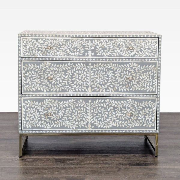 Gray dresser with handcrafted bone inlay floral design and three drawers on a sleek metal base.