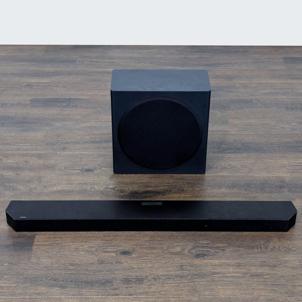 Black Samsung audio equipment set featuring a slim soundbar and cube subwoofer, shown from above.