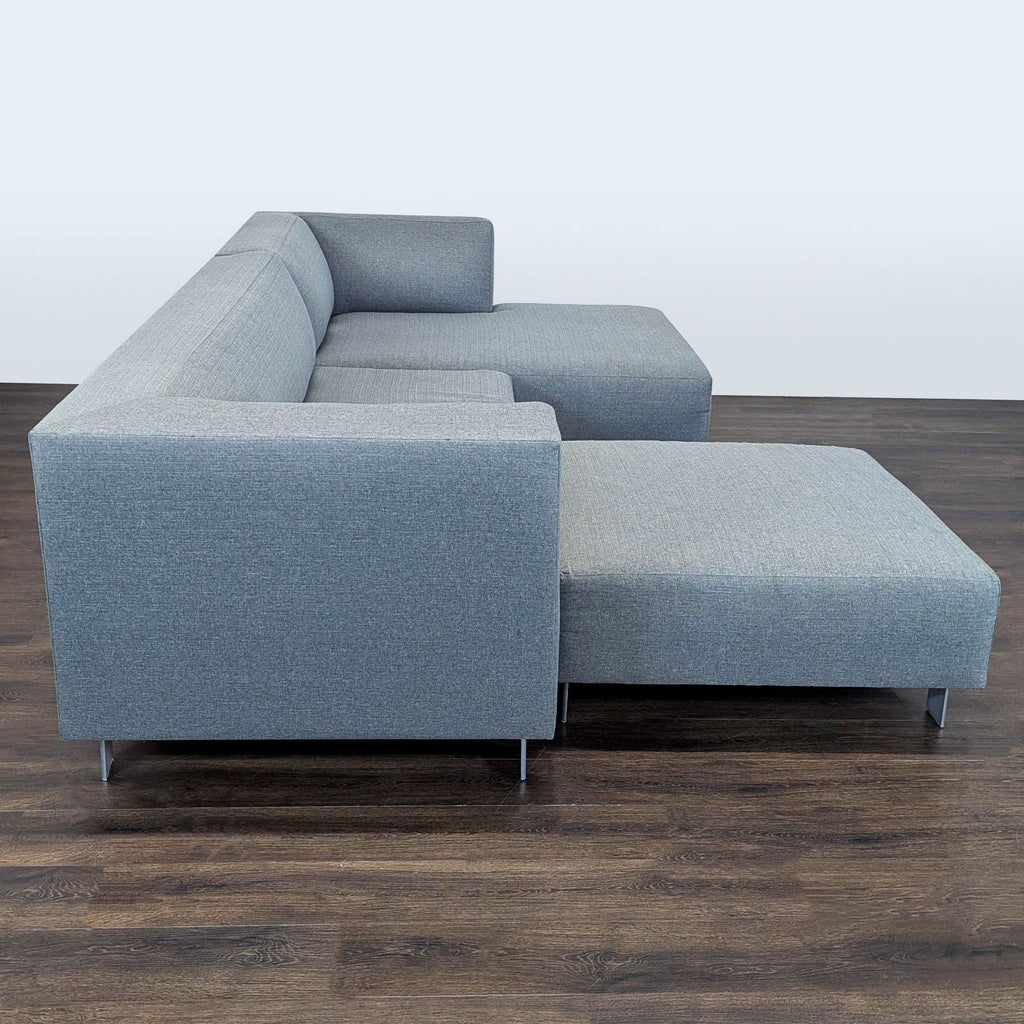 3. Sleek Room and Board sectional sofa, versatile gray upholstery, low arms, metal legs, and matching ottoman from side view.