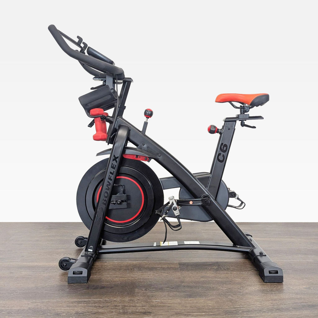 Side view of the Bowflex C6 indoor exercise bike, featuring adjustable seat and red dumbbells on the frame.  