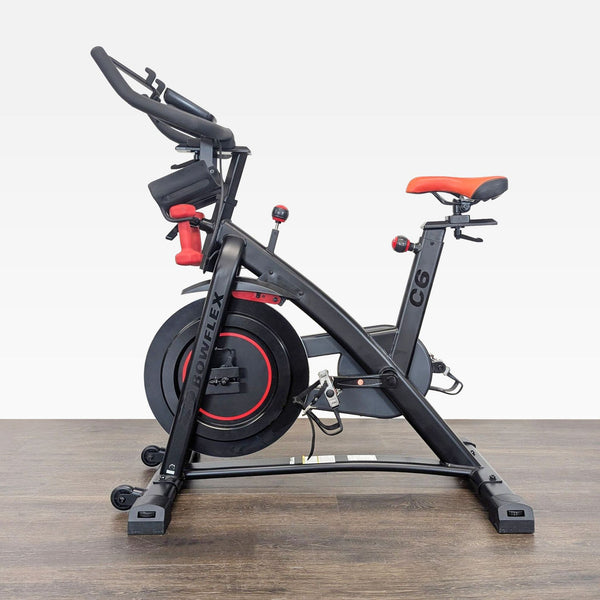 Side view of the Bowflex C6 indoor exercise bike, featuring adjustable seat and red dumbbells on the frame.  