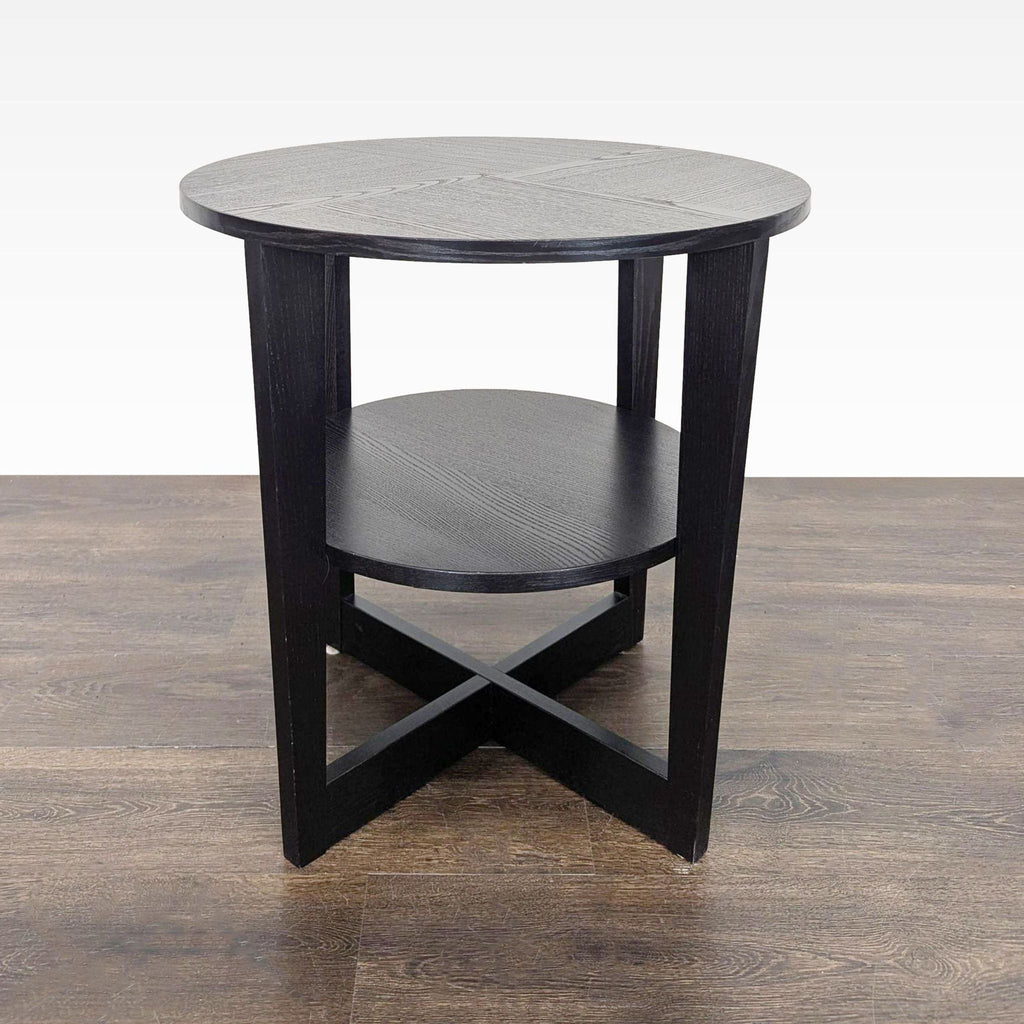 1. Round black wooden end table with lower shelf and crisscross base, shown on wood floor.