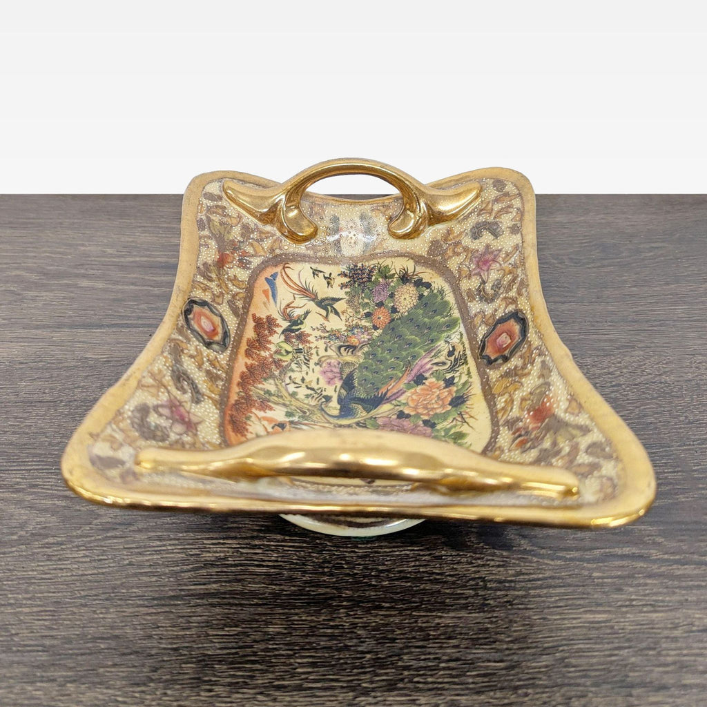 Ornate dish with raised enamel peacock and flowers, gold-gilded handles, and textured surface detailing.