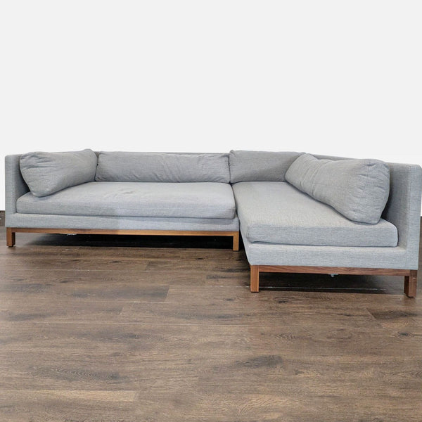 Modern Interior Define sectional in soft grey fabric with L-shape, walnut wood base, and spacious seating.