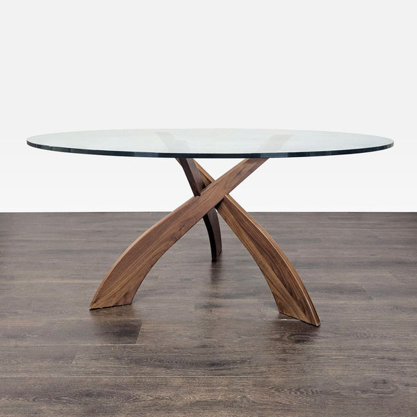 1. Round glass dining table with sculptural wooden crossed legs, shown on a dark wood floor.