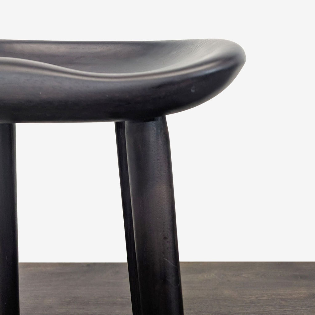 3. Close-up of a dark wooden stool's contoured seat and rounded leg, showcasing smooth craftsmanship.