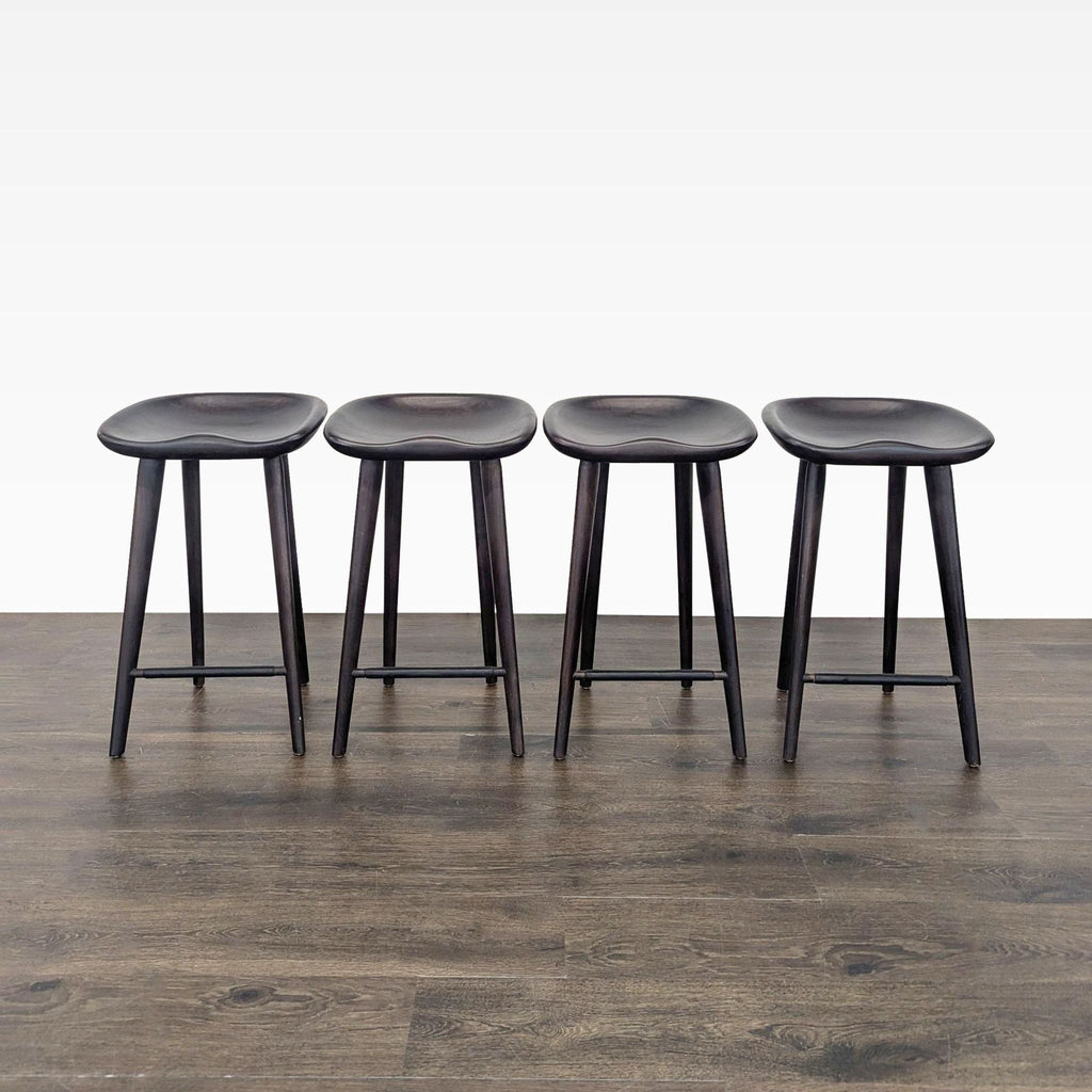 1. Set of four dark wooden stools with contoured seats and round legs, arranged in a row on wood flooring.  