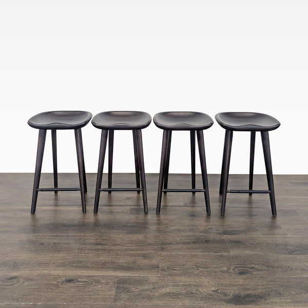 1. Set of four dark wooden stools with contoured seats and round legs, arranged in a row on wood flooring.  