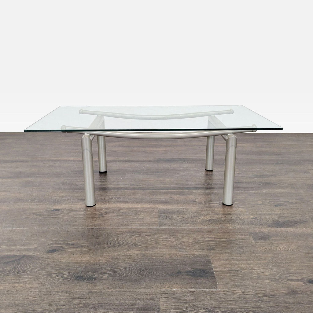 3. Rectangular glass coffee table with sturdy cylindrical silver legs, placed on dark wood flooring.