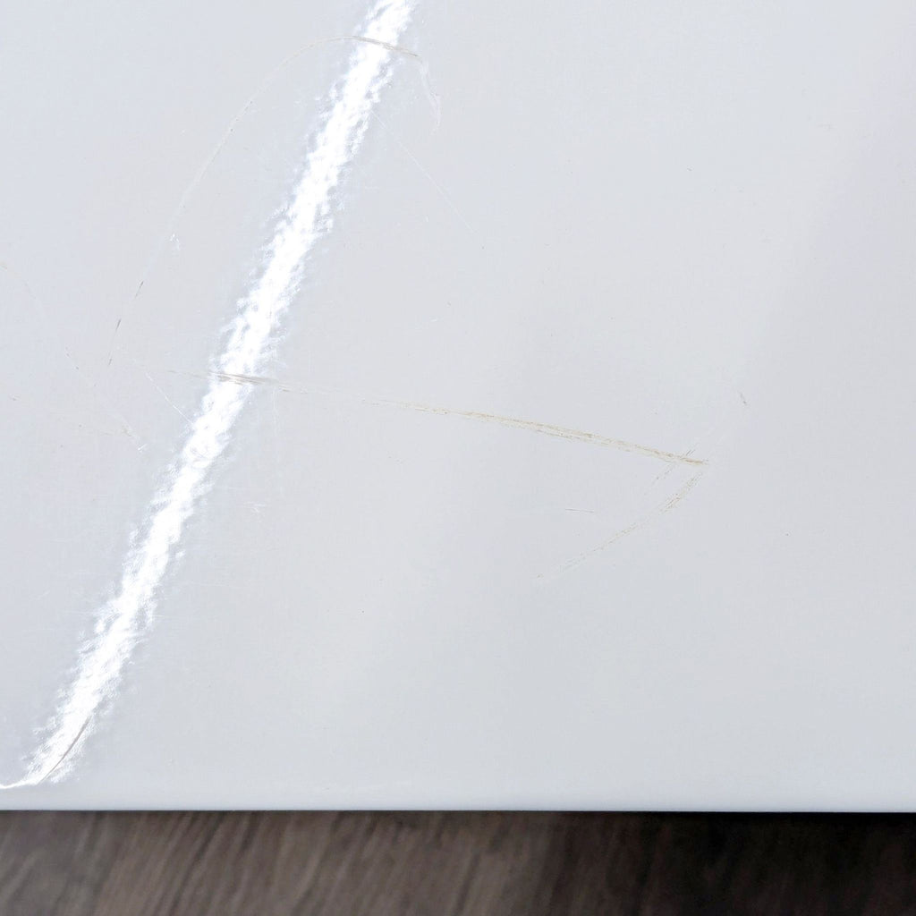 Detail of coffee table surface showing visible scratches and scuff marks on white finish.