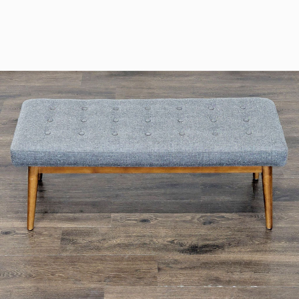 2. Top view of a West Elm gray cushioned bench with button tufting and mid-century wooden legs, used as an ottoman or bench.