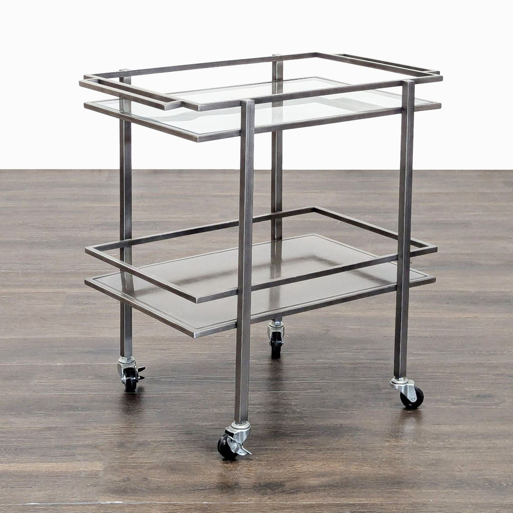 3. Angled view of a minimalist two-tier glass and metal serving cart with wheels, on a wood floor.
