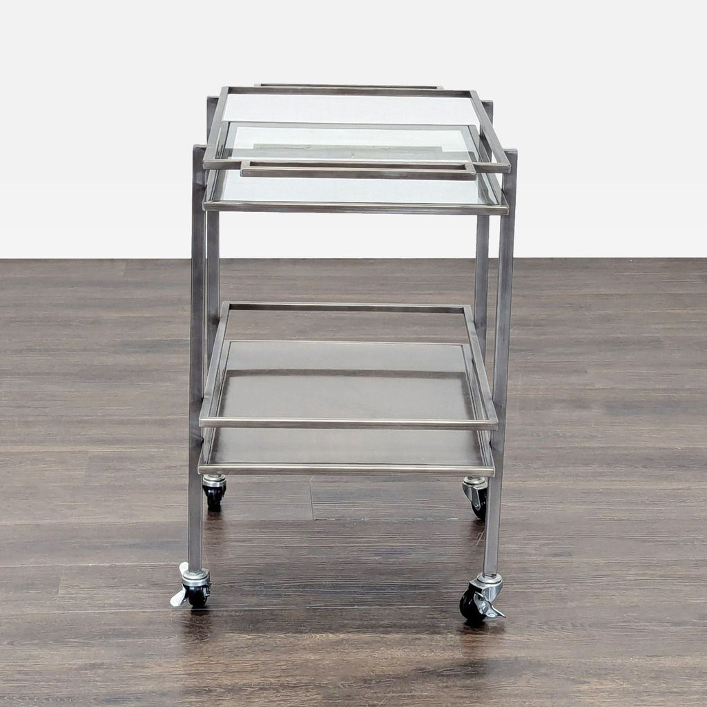 2. Side view of a modern metal-framed cart with glass shelves and caster wheels on a wood floor.