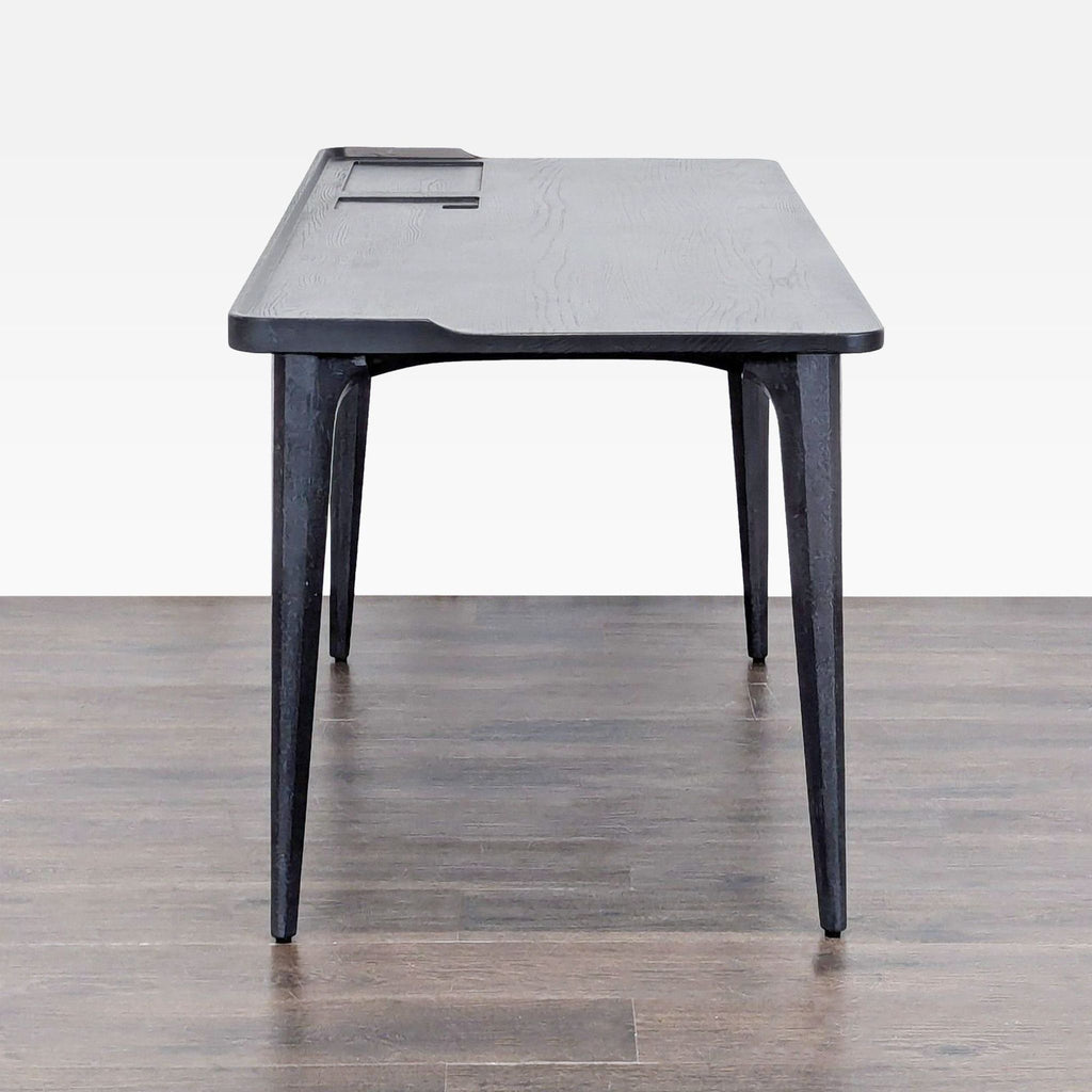 3. Contemporary black desk from District Eight, showing raised edge and stable legs on a dark wooden floor.