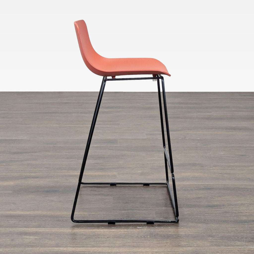 1. Modern Article bar stool with a coral seat and black metal base, side view on wood flooring.
