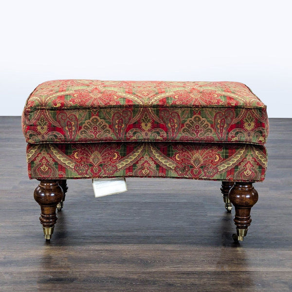 1. Upholstered Lillian August ottoman with red and green patterned fabric, turned wood legs, and brass casters.