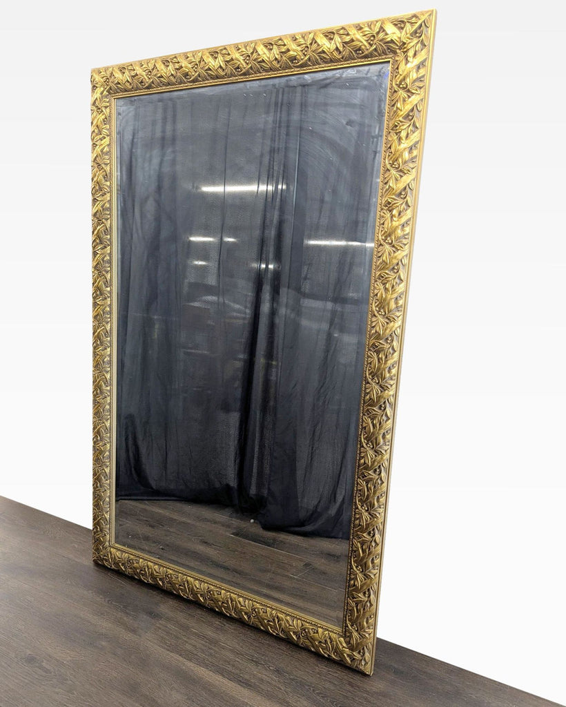 2. Large vertical mirror with intricately carved gold border, shown from a side angle on a wood surface.