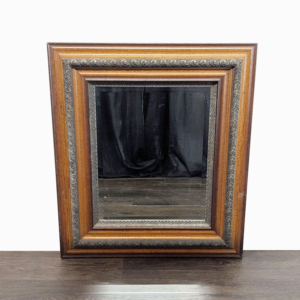 1. Rectangular framed mirror with ornate wood and metal detailing, leaning against a dark wood floor background.