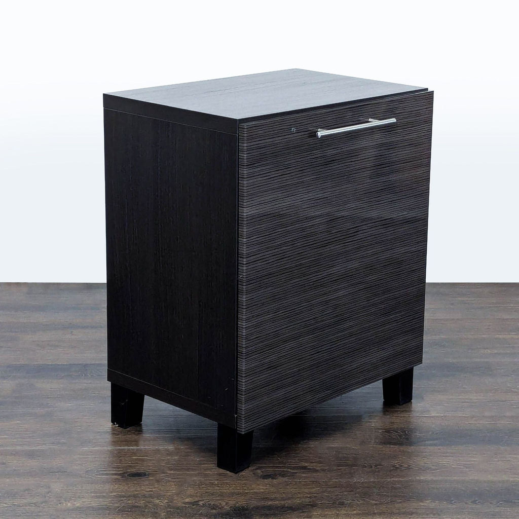 3. Angled view of a dark wood cabinet with a metal handle and elevated legs, shown on wood flooring.
