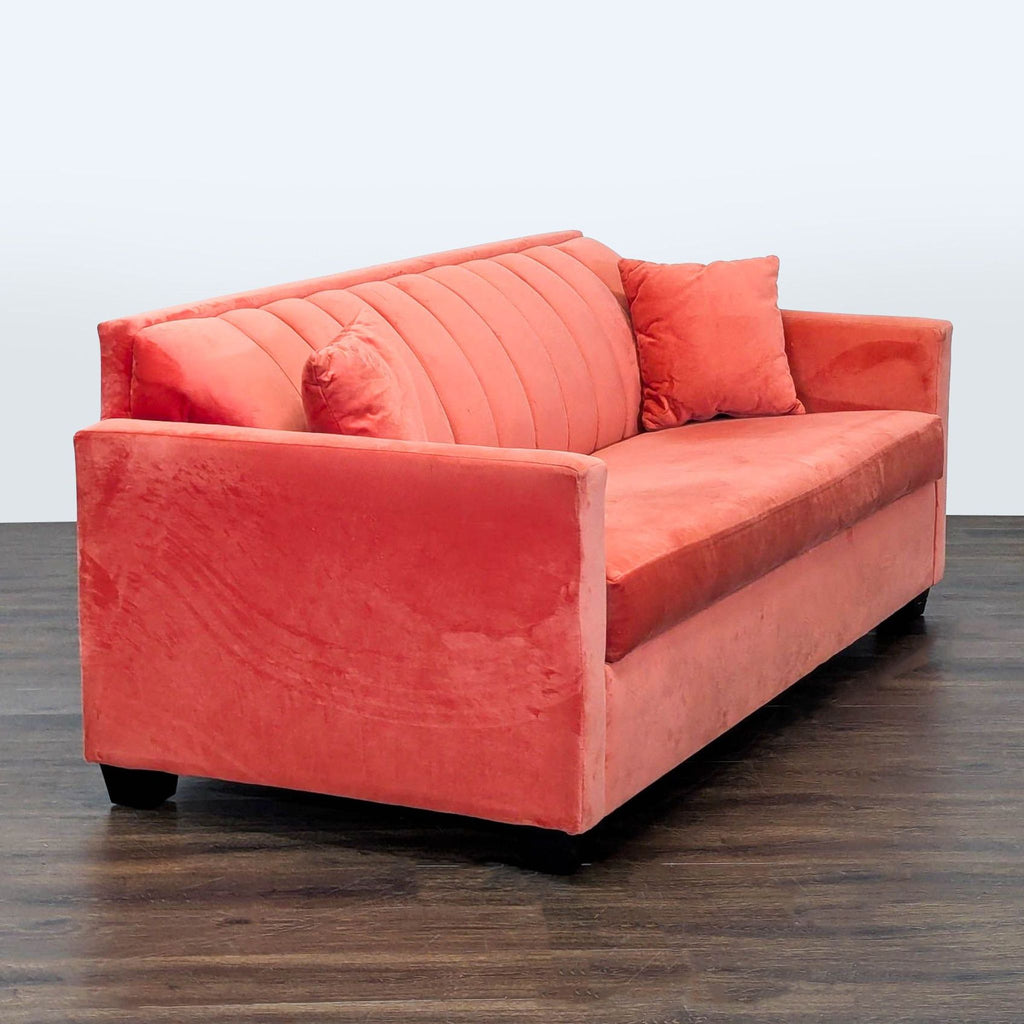 Coral velvet sleeper sofa with sleek silhouette, comfortable seating, and two matching throw pillows for extra coziness.