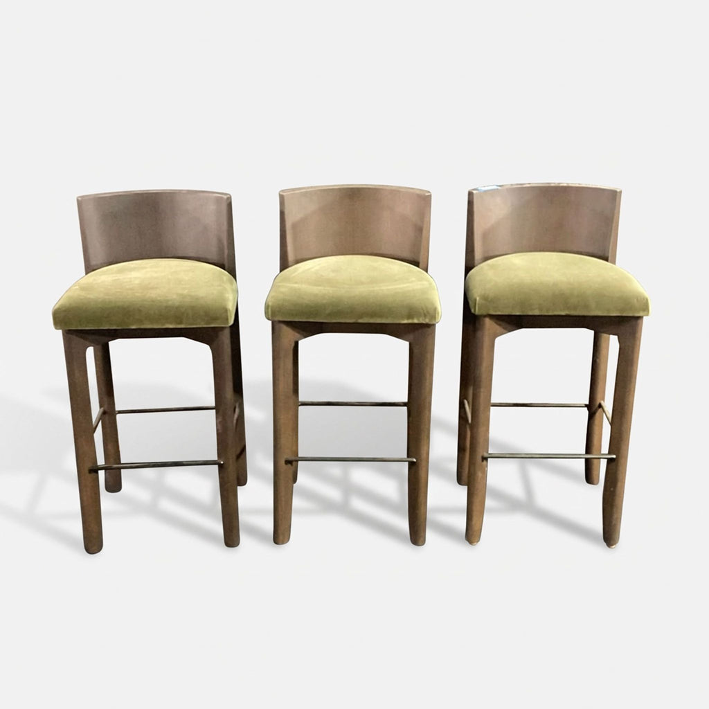 A set of three Maiden Home Delancey bar stools with curved wood backs, green upholstered seats, and metal footrests.  