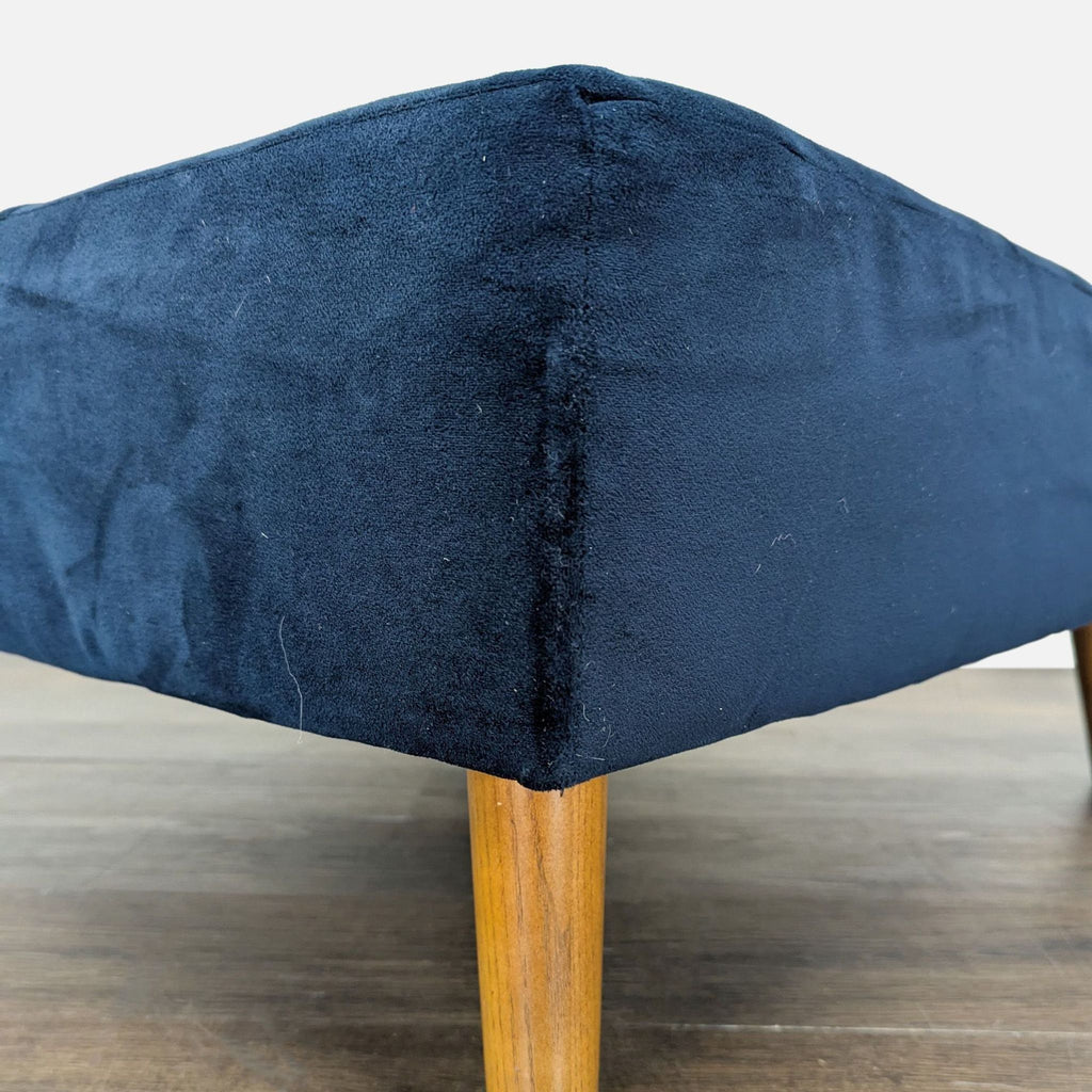2. Close-up of a navy blue ottoman corner with textured fabric and tapered wooden leg.