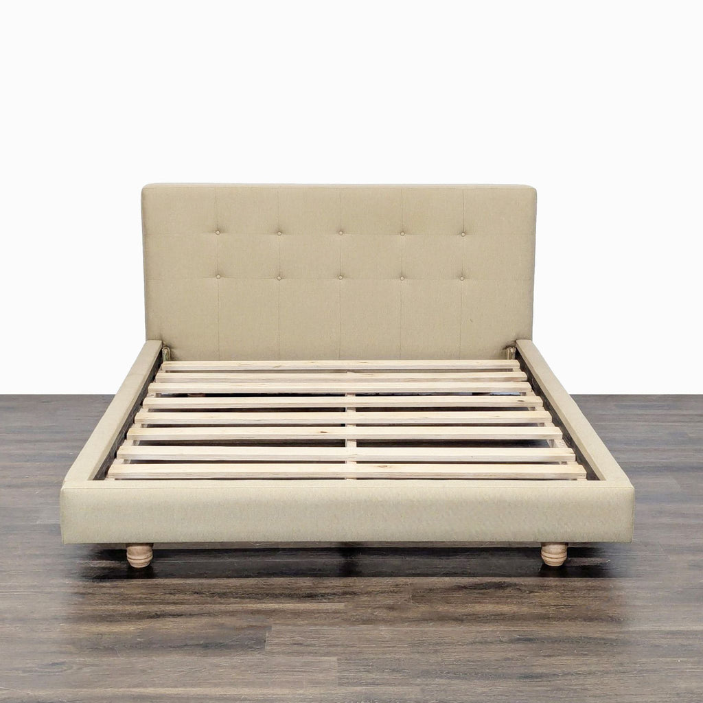 1. Beige Crate & Barrel bed frame with tufted headboard, wooden slats, and turned legs, viewed from the front.
