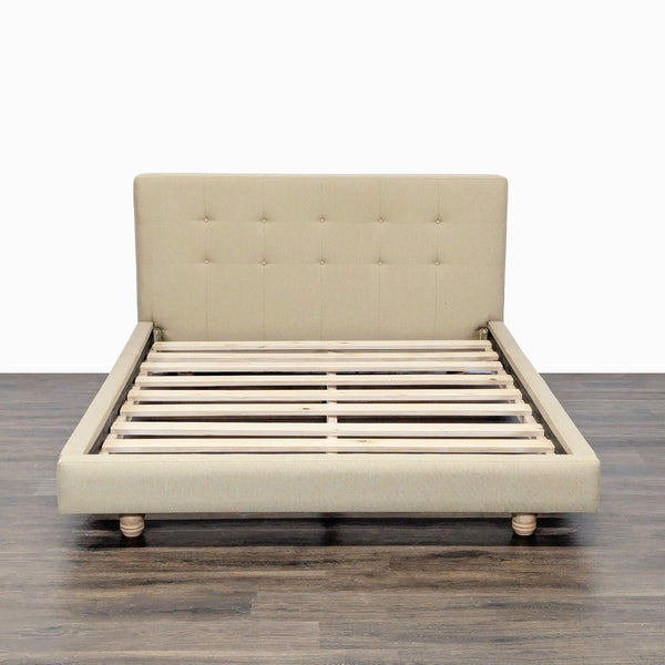 1. Beige Crate & Barrel bed frame with tufted headboard, wooden slats, and turned legs, viewed from the front.