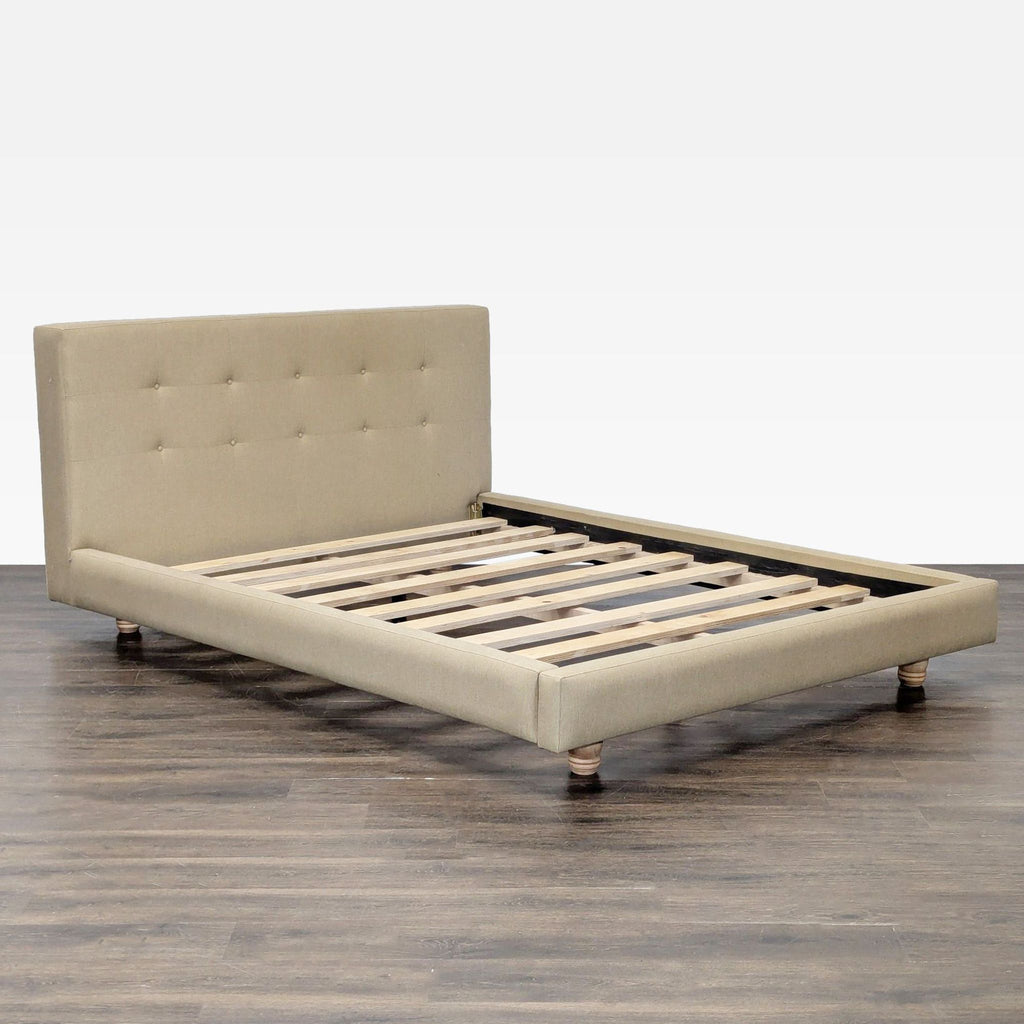 2. Angled view of a modern beige upholstered bed frame by Crate & Barrel, showing wooden slats and low-profile design.