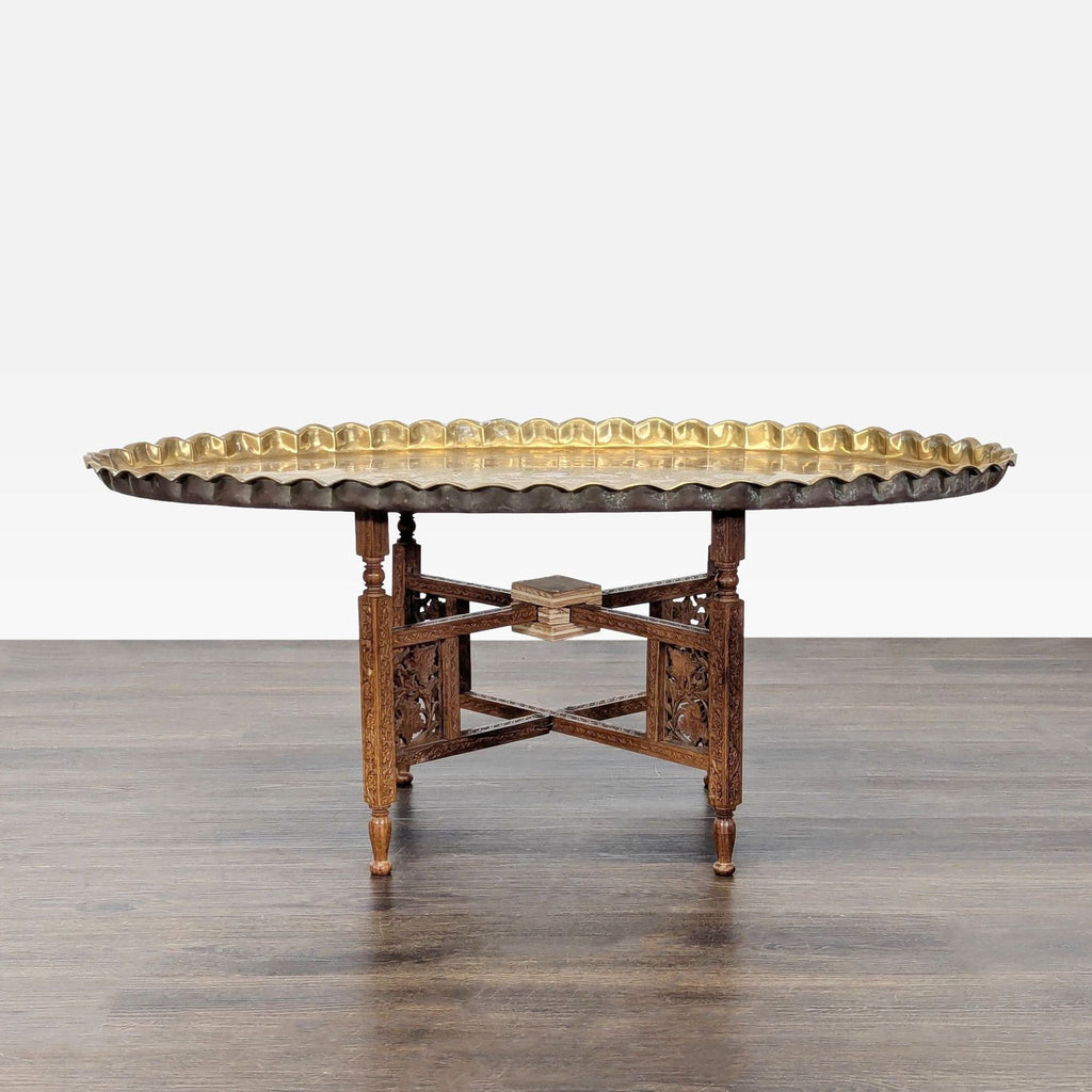 Brass etched coffee table with foliate designs, pie-crust edge, on a carved, folding wooden stand.