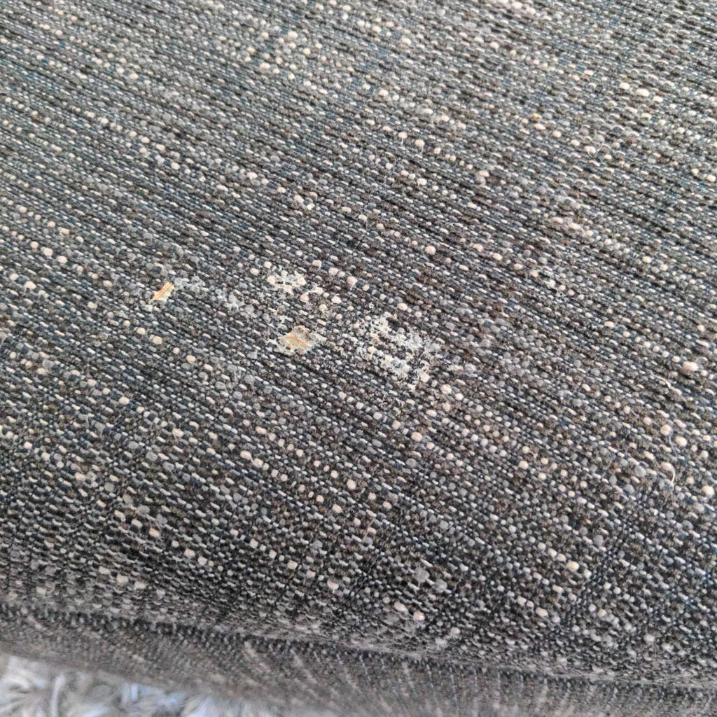 3. Close-up of the ottoman’s fabric showing visible wear and surface damage on the upholstery.
